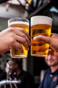 Common Things That Cause Regret in Old Age and How to Avoid Them 4 Close-up of two friends toasting with cold beer glasses at a lively bar, celebrating friendship and good times.