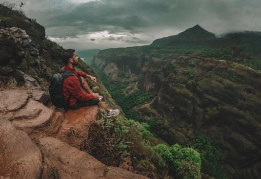 The Hidden Power of Stillness: Why Doing Nothing Can Change Everything 4 A man sits on a cliff edge, enjoying the scenic view of lush mountains and dramatic cloudy skies.
