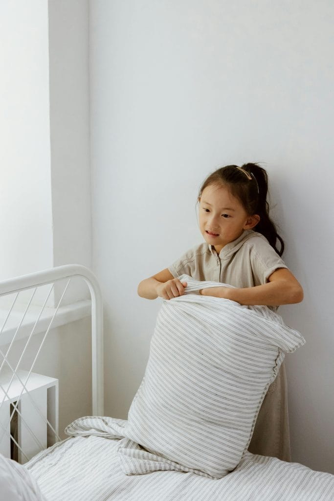 Essential Life Skills to Teach Kids: Building Confidence and Independence from Toddler to Teen 5 A young girl making a bed in a bright, minimalistic room, showcasing daily chores.