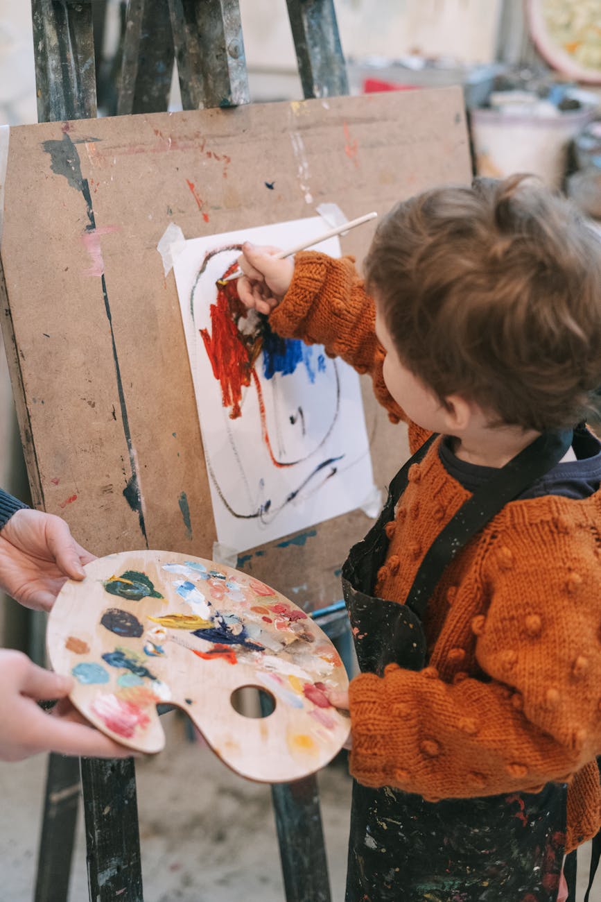 boy in orange and black sweater painting on white board