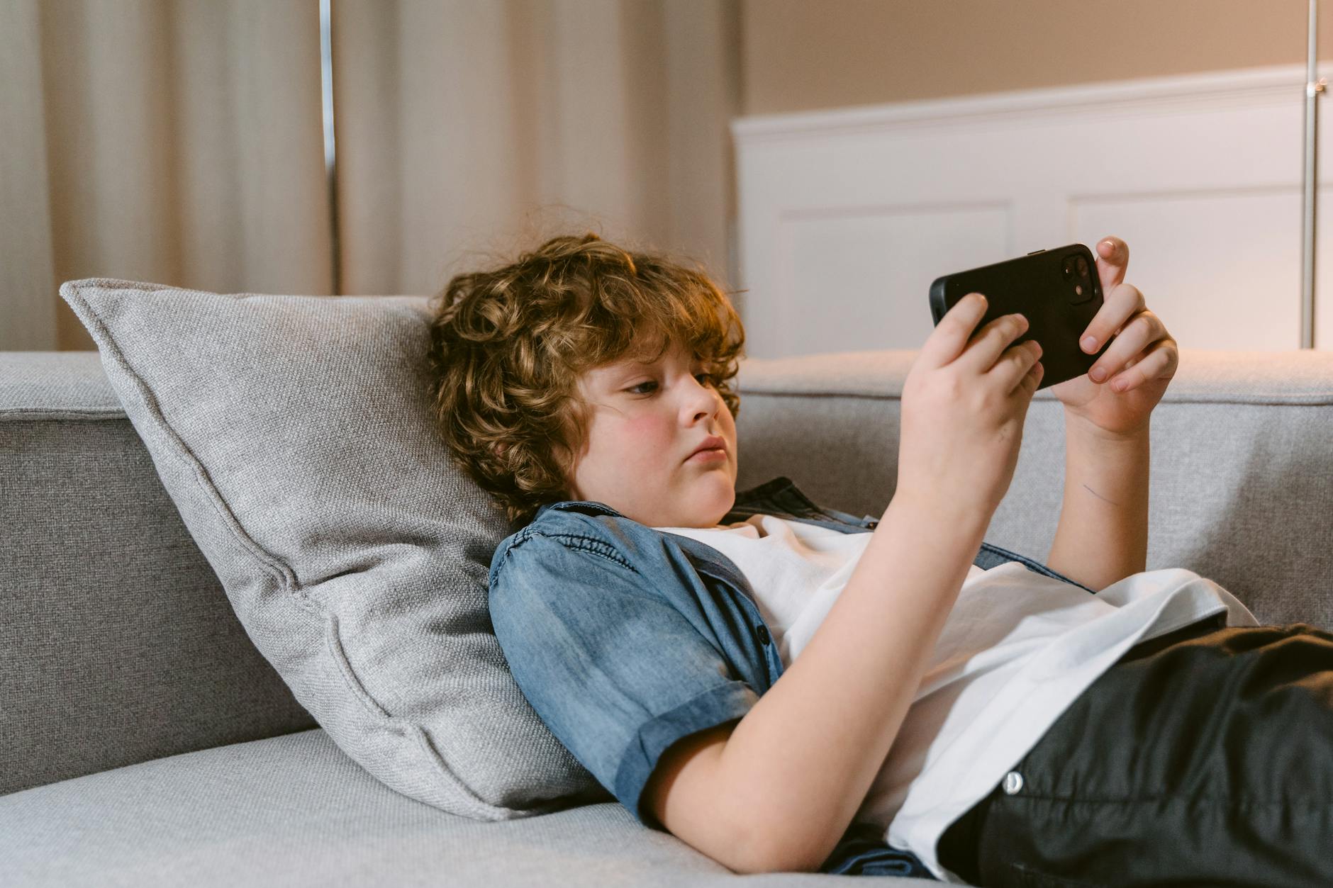 Essential Life Skills to Teach Kids: Building Confidence and Independence from Toddler to Teen 7 a boy using a smartphone while lying on a sofa