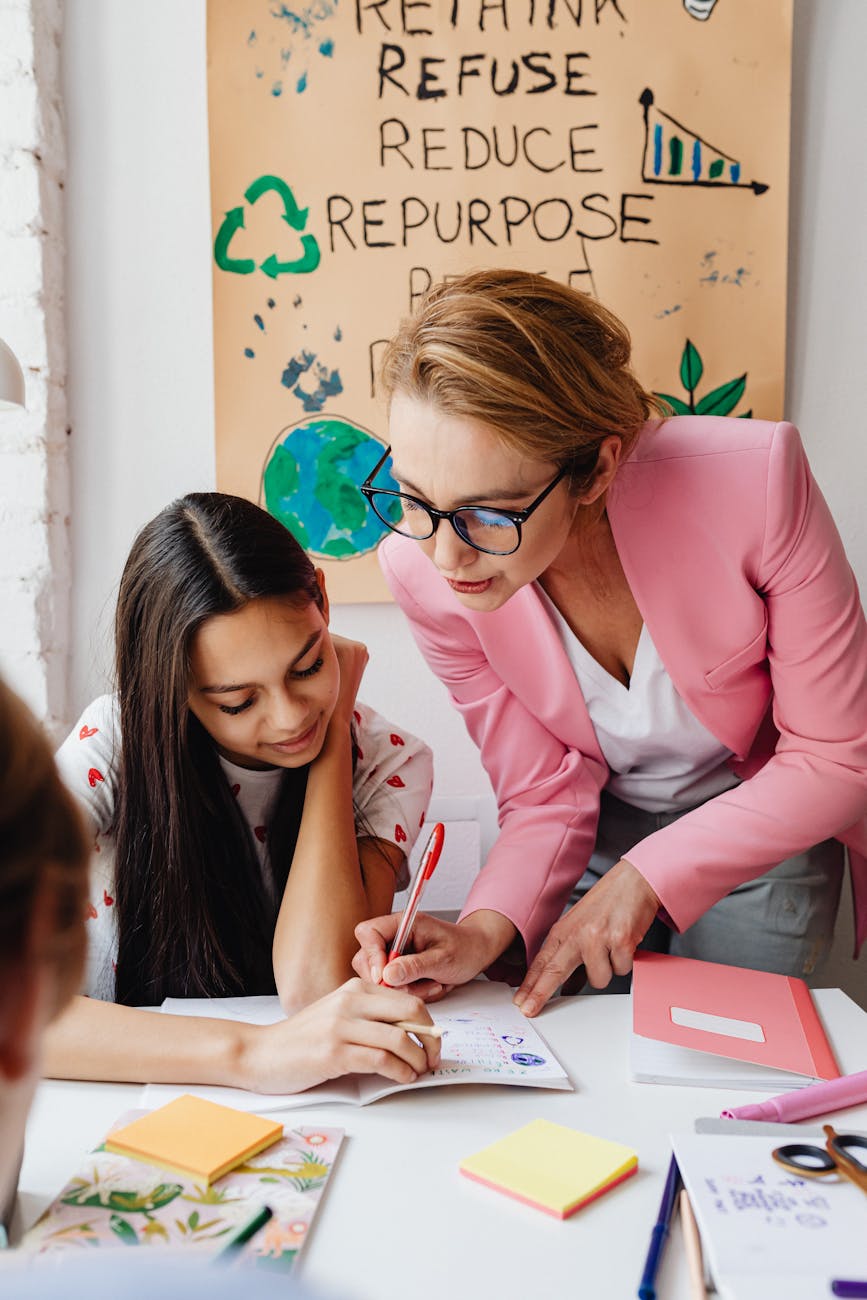 a woman in pink blazer writing on a notebook beside a young woman
